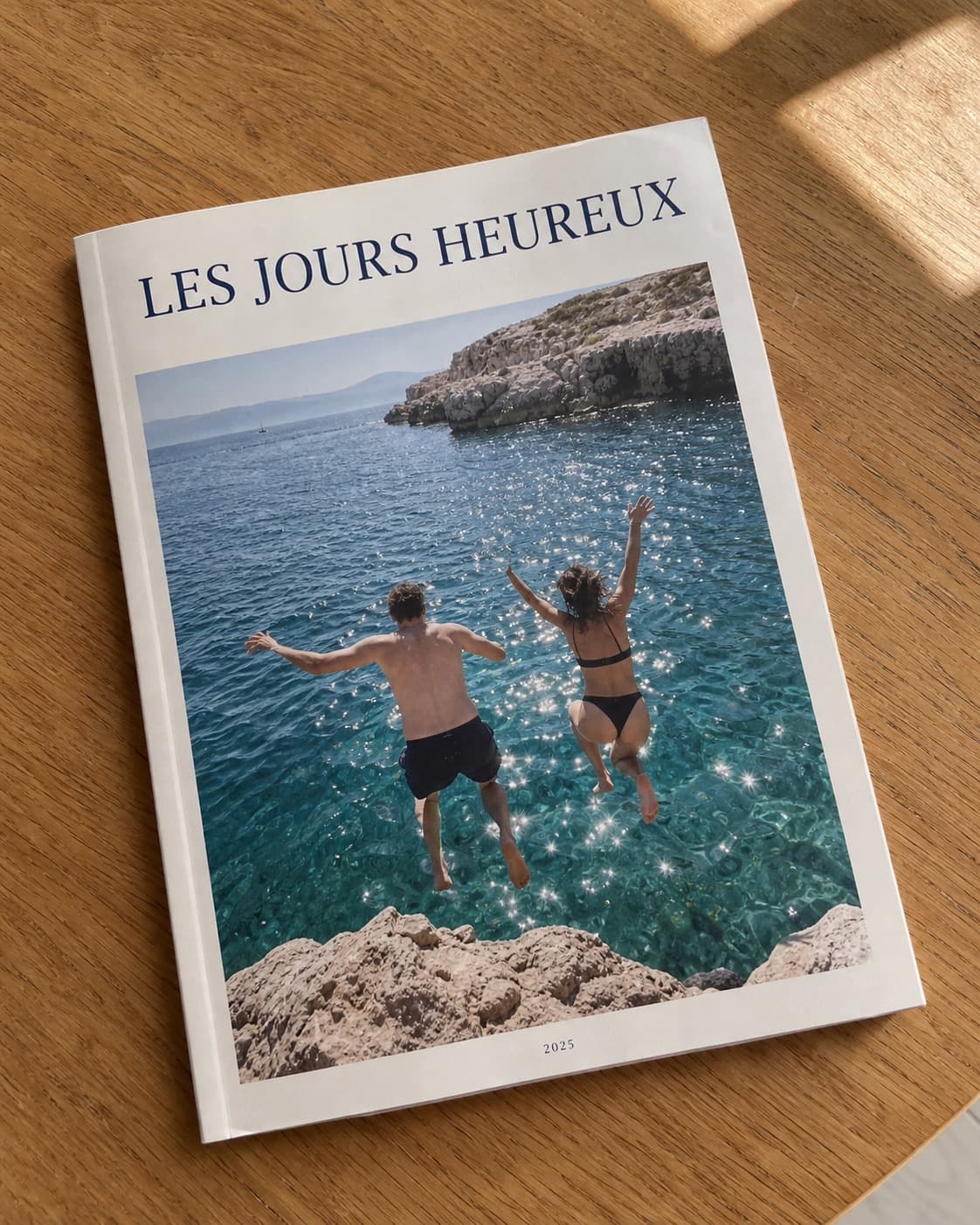 Magazine photo « Les jours heureux » posé sur une table en bois, deux personnes sautent dans la mer en couverture
