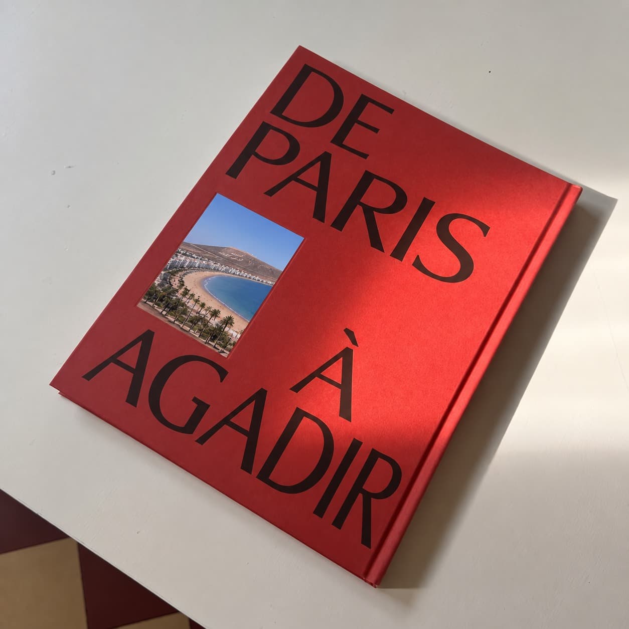 Livre photo à couverture rigide rouge « De Paris à Agadir » posé sur une table blanche